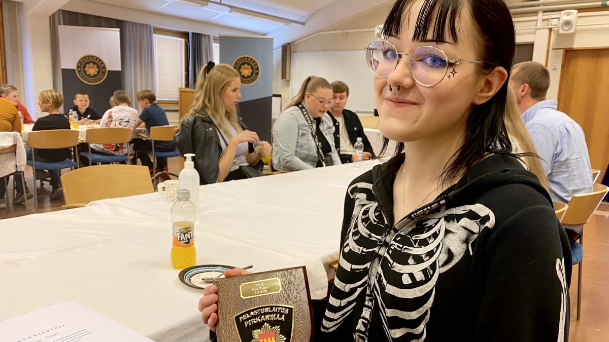 Tyttö pitelee kädessä pelastuslaitoksen ansiomerkkiä.
