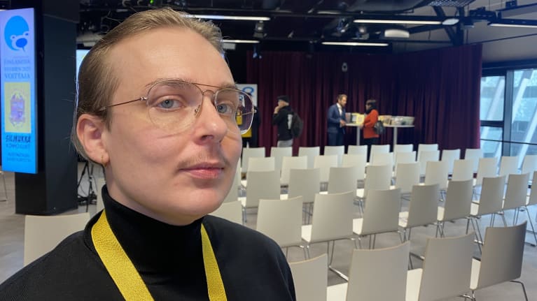 Silmälasipäinen Kimmo Lust katsoo kohti kameraa. Taustalla näkyy tyhjiä penkkirivejä.