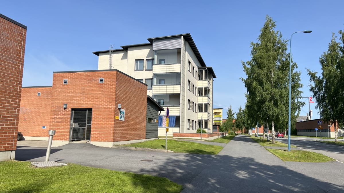 Tiilinen roskakatos, jonka takana valkea kerrostalo. 
