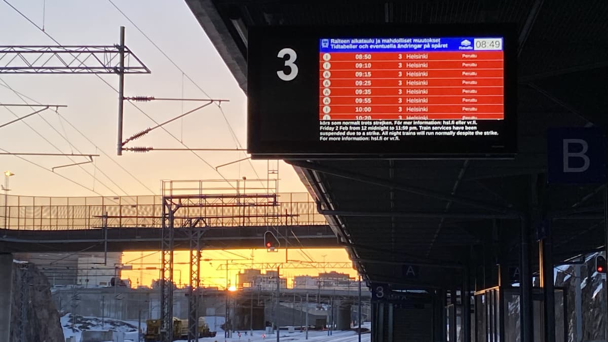 Ilmalan juna-asemalla Helsingissä oli hiljaista perjantaiaamuna. Taustalla HSL:n näyttötauli punaisena ja auringon kajo.