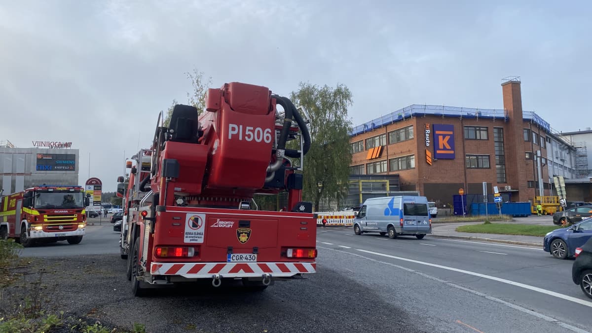 Paloautoja punatiilisen rakennuksen edessä. Rakennuksen kyljessä on K-raudan kyltti.