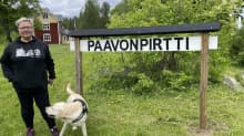 Nainen ja koira seisovat talon pihanmaalla.