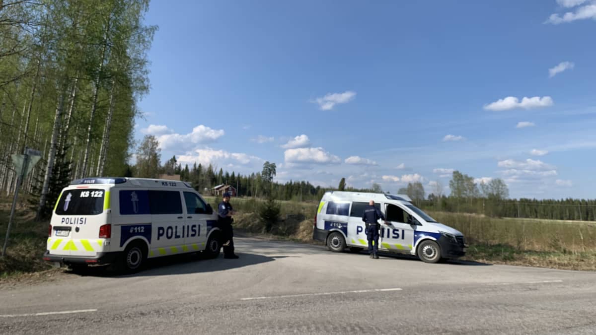 Kaksi poliisiautoa pysäköitynä hiekkatien varteen.