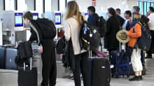 Ihmisiä lentokentällä matkalaukkujen kanssa jonottamassa matkalaukkujen jättämiseen.