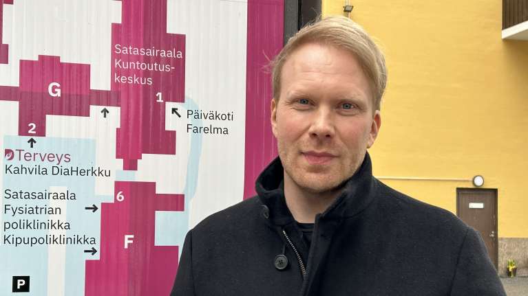 Vaalea aikuinen mies, Toivu riippuvuudesta -hankkeen projektipäällikkö Kalle Mäenpää, taustallaan Diakonialaitoksen opastaulu ja keltainen seinä.