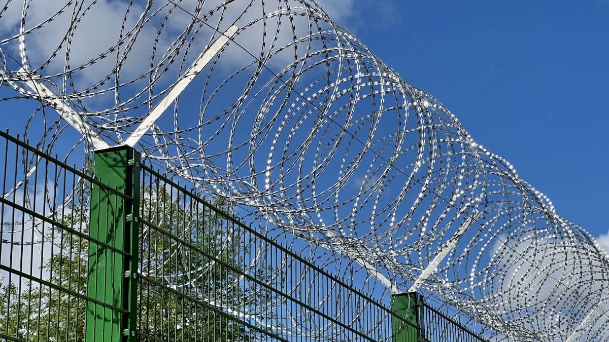 Photo shows a section of the 4-metre-tall border fence with barbed wire on top.
