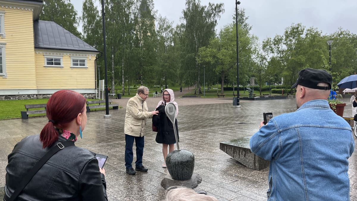 Mies ja nainen poistavat kankaan taideteoksen päältä. Taideteos näyttää poijulta ja siinä on qr-koodi.