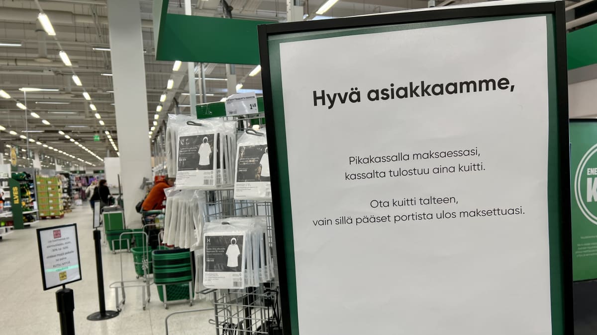 Kyltti Tampereen Lielahden Prismassa, jossa kerrotaan, että pikakassalta saatu kuitti pitää säilyttää. Taustalla näkyy markettiympäristöä. 