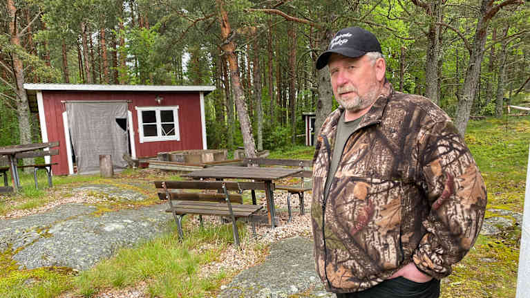 En man som står vid några piknickbord och ett vedlider i en skog.