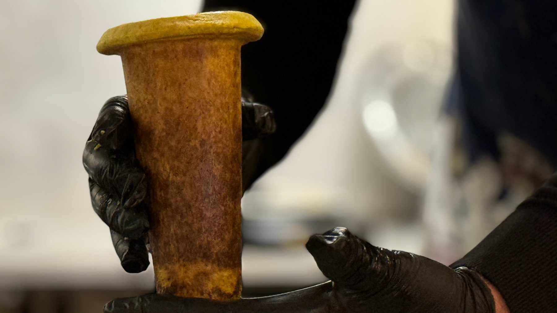 a man`s hand holding freshly made soup in an edible bread cup.