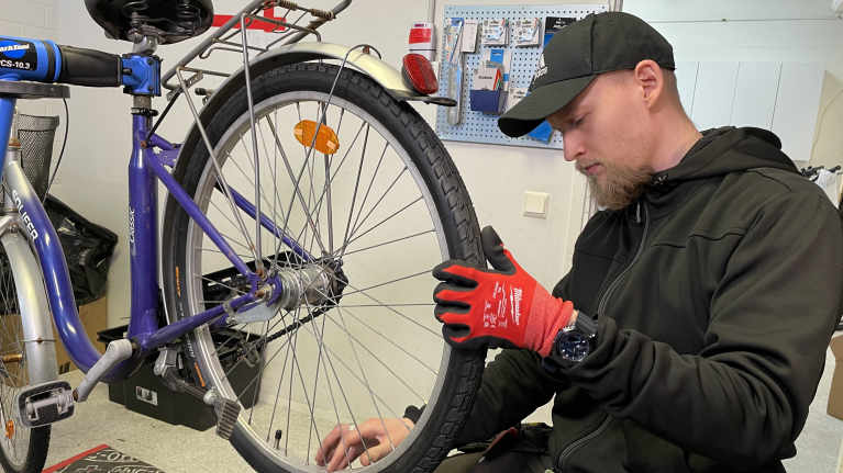 Lippalakkipäinen mies asentaa pyörän takapyörää.