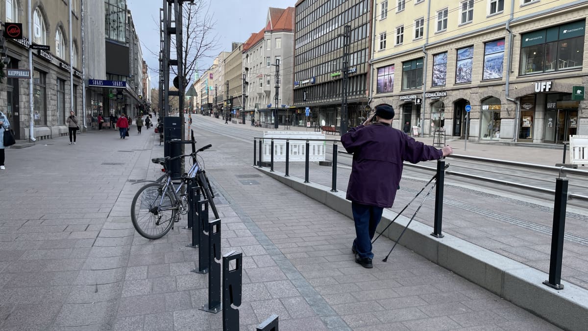 Ihminen nojaa kaiteeseen ja seisoo keskellä pyörätietä Tampereen Hämeenkadulla. 