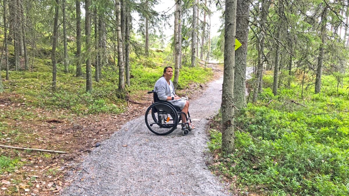 Nainen istuu pyörätuolissa metsäpolulla
