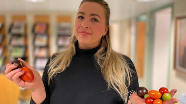 En kvinna med svart tröja står och håller i tomatar i sina händer.