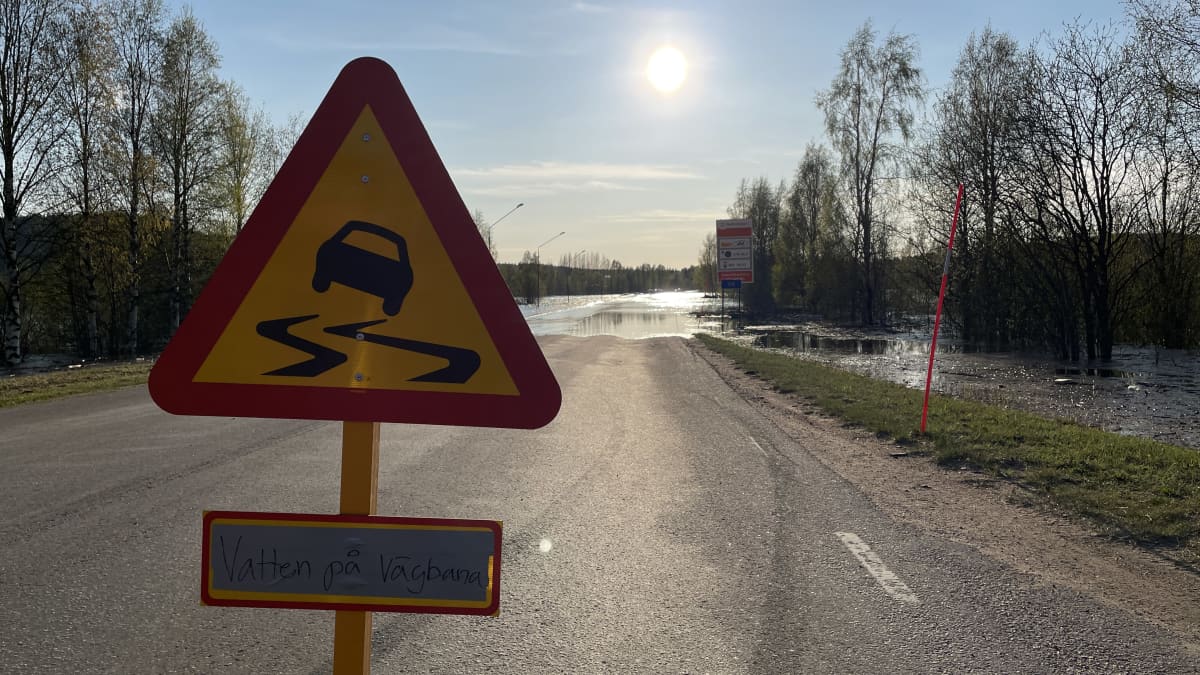 Kuvassa on liikennemerkki, joka varoittaa, että tiellä on vettä. Taustalla näkyy Suomen ja Ruotsin raja.