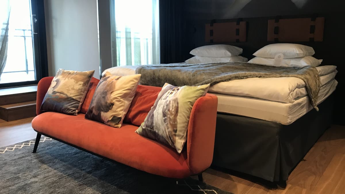 Uudistettu hotellihuone, jossa on punainen sohva ja muhkea sänky.