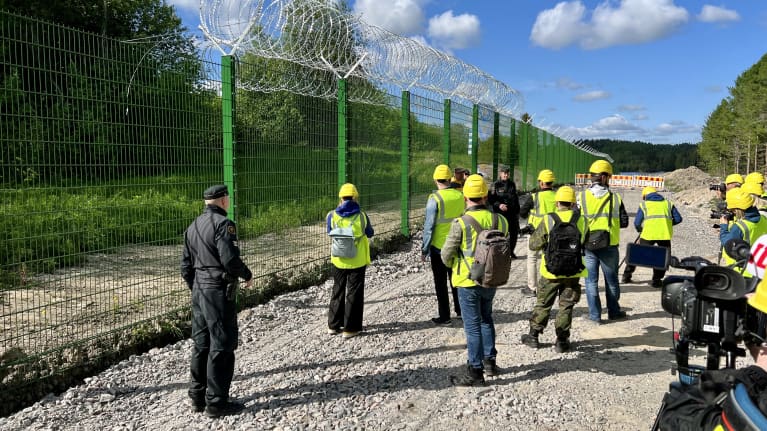 Huomioliiveihin ja kypäriin pukeutuneet median edustajat tutustuvat aitatyömaahan rajavartioston opastuksella.