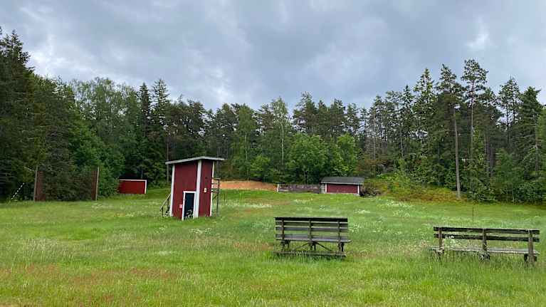 En gräsmatta med små röda byggnader för att öva lerduvsskytte och kulskytte.