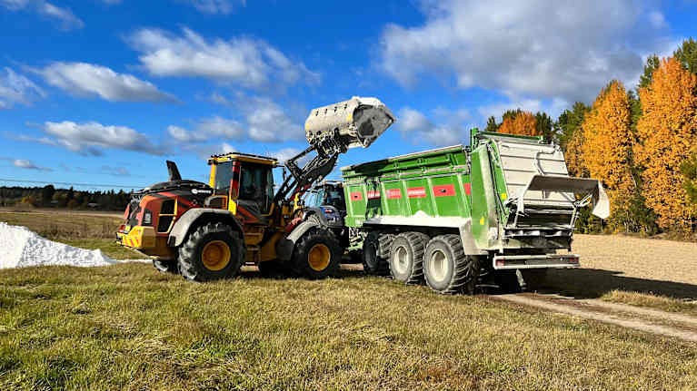 En traktor skopar upp gips på en vagn som sedan ska spridas ut på en åker.