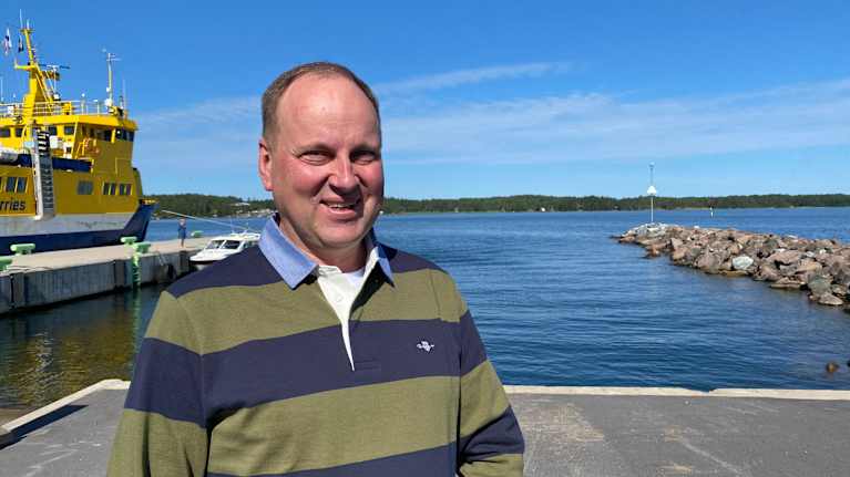 En man som står vid havet. I bakgrunden en gul förbindelsebåt.
