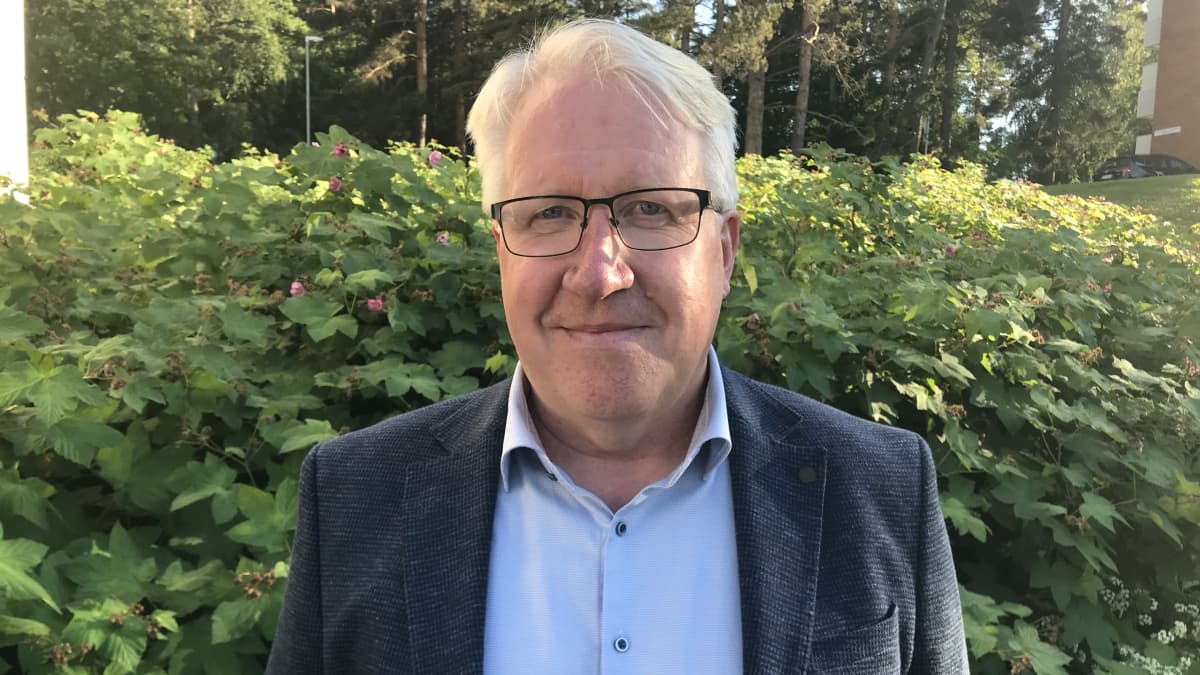 Sinipaitainen ja harmaapäinen mies hymyilee kameralle.