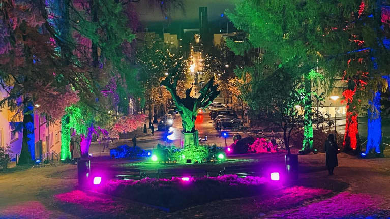 Monenkirjavia jouluvaloja, vihreällä valolla värjätty patsas ja pitkä kaupungin raitti taustalla.