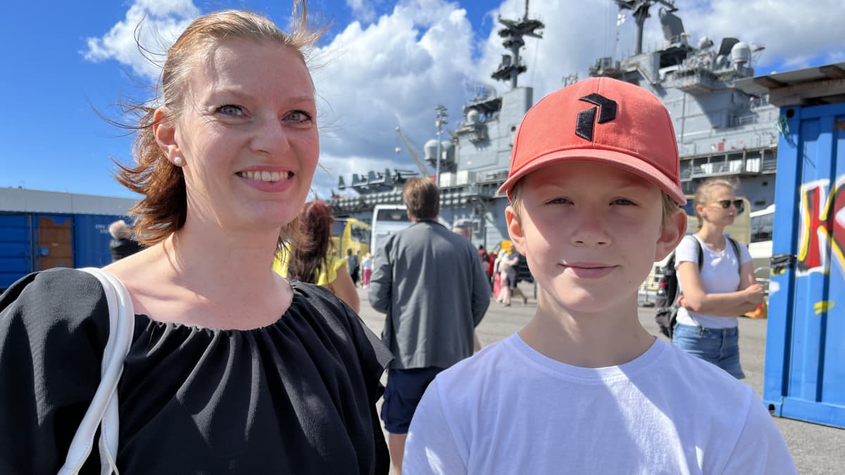 Espoolaiset Anne ja Onni Laitinen, taustalla muita ihmisiä ja Yhdysvaltain maihinnousutukialus Kearsarge.