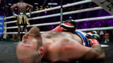 Robett Helenius makaa tyrmättynä kanveesissa. Deontay Wilder taustalla juhlimassa voittoa omassa kulmauksessaan.