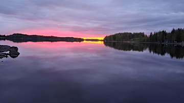 Kesäilta järven rannalla: auringonlaskun hehkua rauhallisen vedenpinnan yllä.