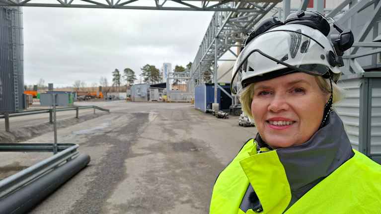 Rauni Karjala, en person i gul reflexjacka och skyddshjälm står utomhus på ett industriområde.