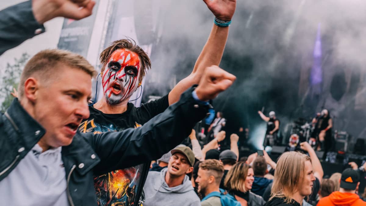 Heavy metal fan wearing face paint holding up his hand and staring into the camera at a gig during the Kuopiorock festival in 2022. 