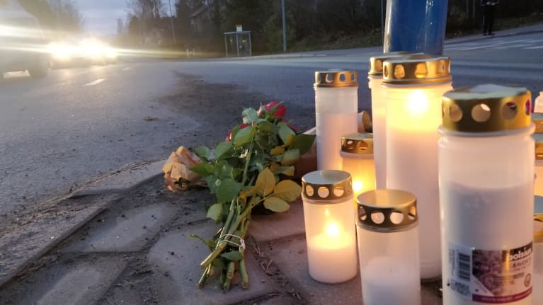 Makeshift memorial by the road at a zebra crossing with car headlights shining in the background at dusk.