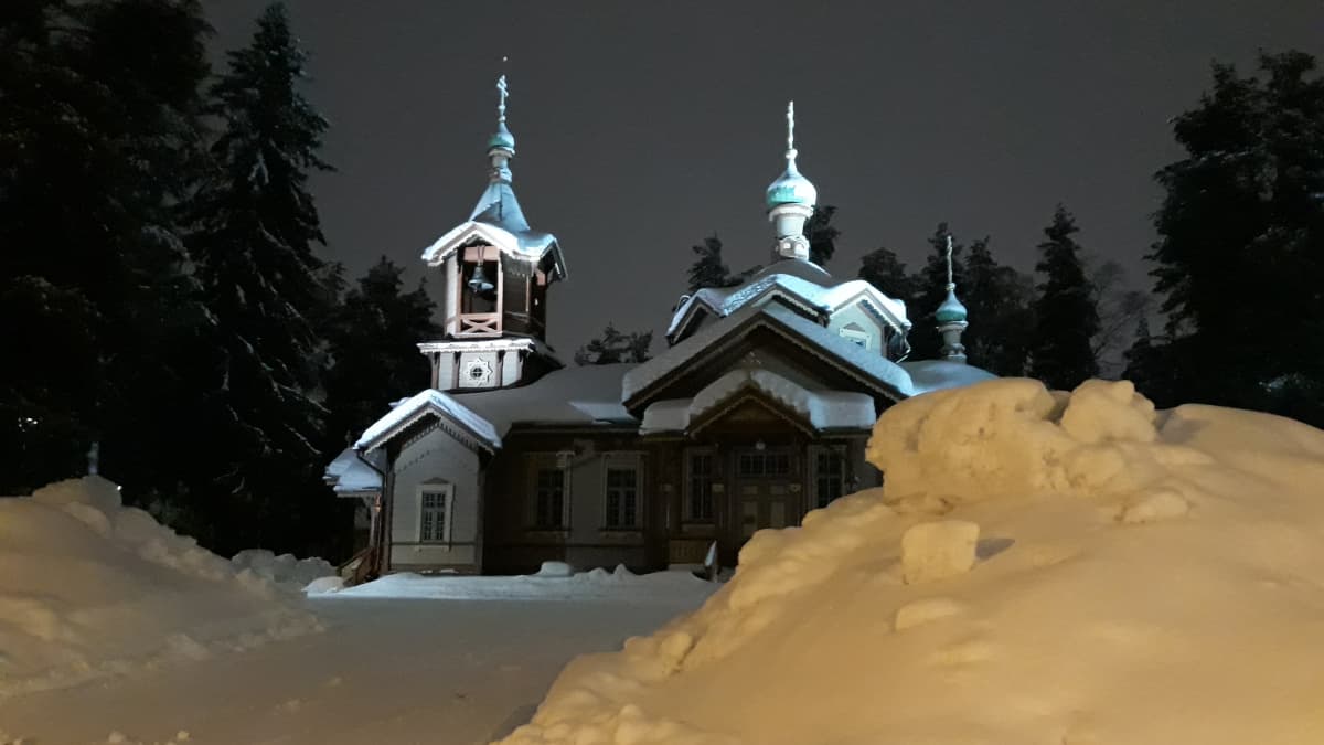 Joensuun ortodoksinen kirkko yövalaistuksessa korkeiden lumipenkkojen ympäröimänä.