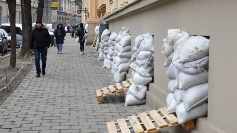Jalankulkijat kävelevät hiekkasäkeillä suojattujen ikkunoiden ohitse Lvivin kaupungissa Länsi-Ukrainassa.