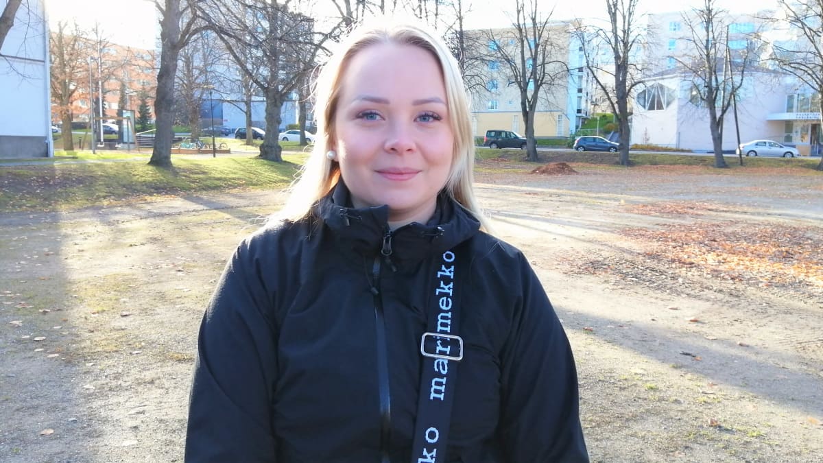 Nuori nainen seisoo musta takki päällä syksyisessä auringonpaisteessa.