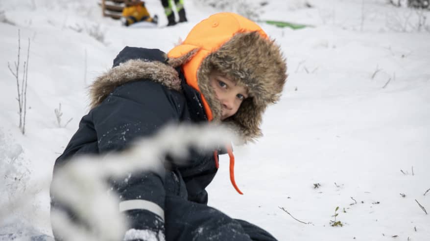 Karvahattuun ja talvivarusteisiin pukeutunut poika laskee mäkeä.