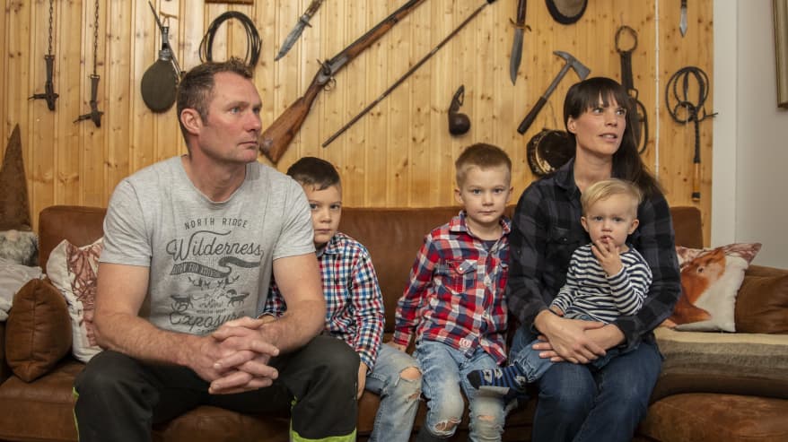 Erkki ja Elin Kinnunen ja heidän kolme poikaansa istuvat sohvalla. Seinälle on ripustettu hirven ja peuran päitä sekä vanhoja metsästysaseita.