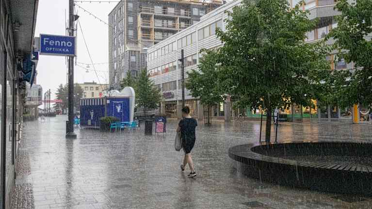 A woman walks down a shopping street in Kouvola during a downpour.