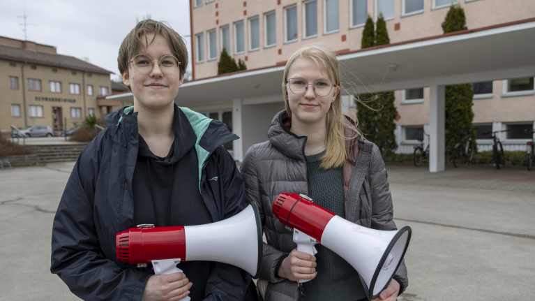 Kaksi oppilasta pitää megafoneja mielenosoituksessa lukion pihalla. 
