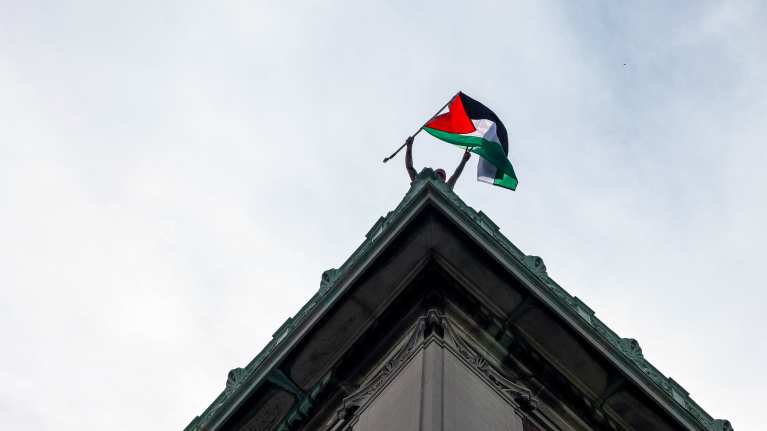 Mielenosoittaja heiluttaa Palestiinan lippua Hamilton Hall -rakennuksen katolla.