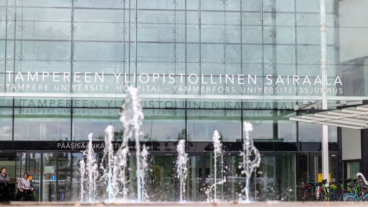 Tampereen yliopistollisen sairaalan pääsisäänkäynti kuvattuna pilvisenä kesäpäivänä. Etualalla suihkulähteestä suihkuavia vesipylväitä.