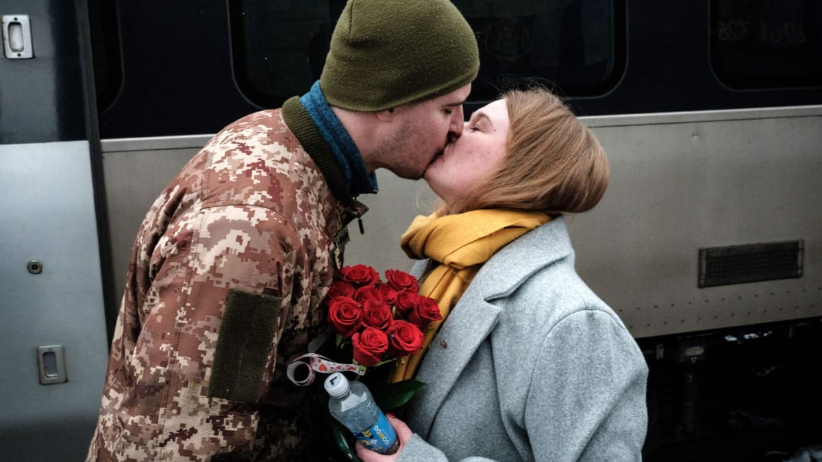 Sotilas ja nainen suutelevat asemalla, naisella kimppu punaisia ruusuja.