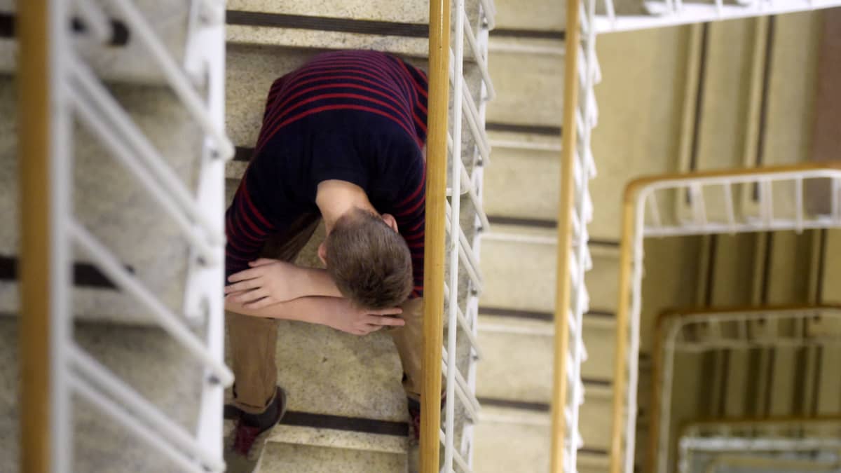 A teenager sitting on a flight of stairs, shot from above.