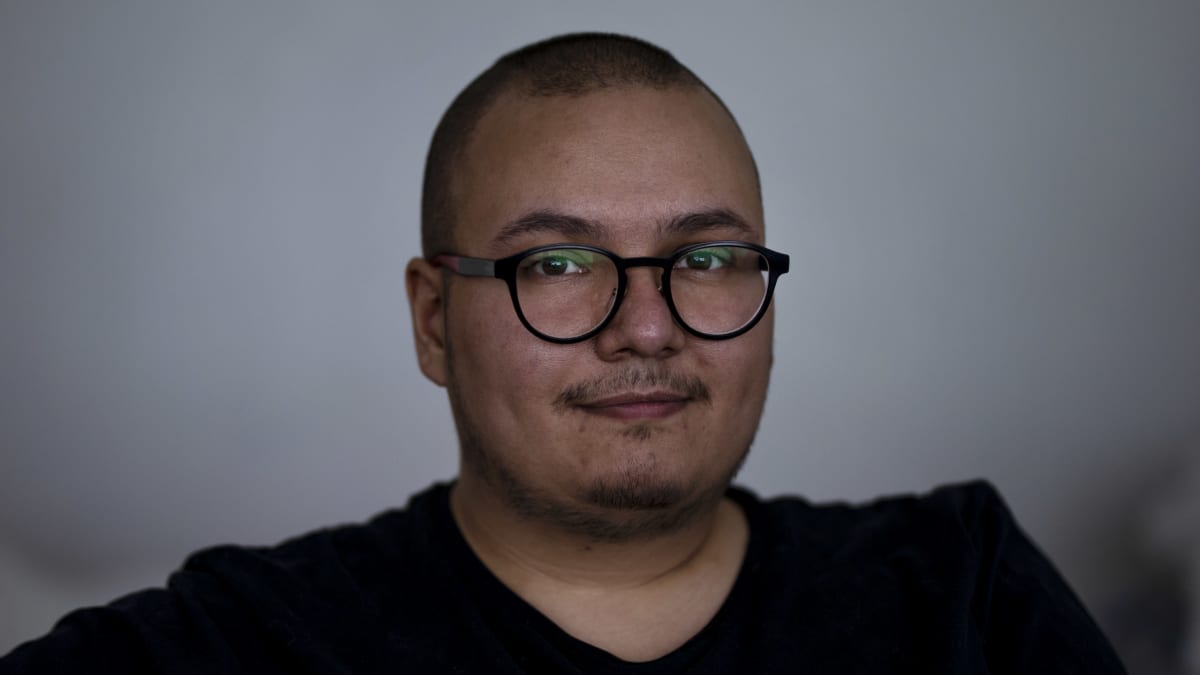 Lähikuva Benjamin Molinista hämärässä huoneessa valkoista seinää vasten. 