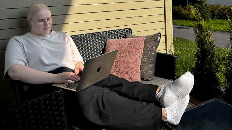 Oona Tammisto sits on the terrace with a computer in her lap.