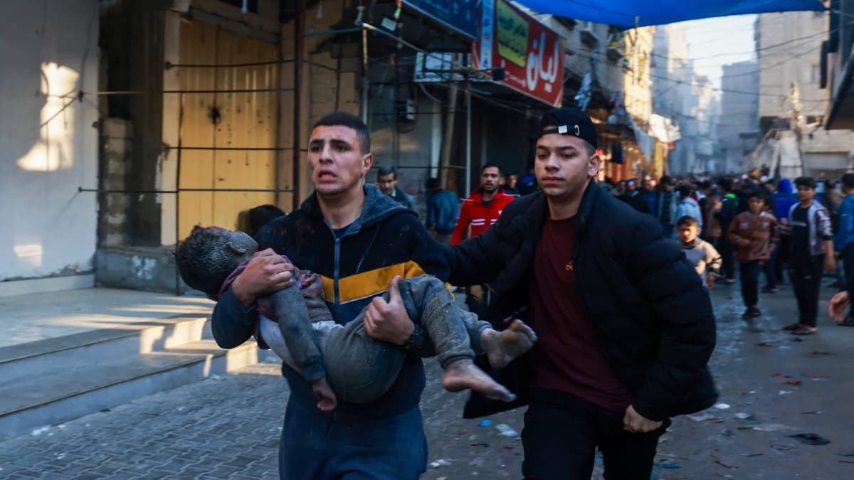 En palestinsk man bär en skadad pojke i Rafah efter att Israel återupptagit flygbombandet mot Gaza 1.12.2023.