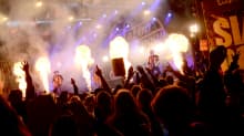 Rock-yhtye esiintyy lavalla, edessä yleisöä nauttii musiikista kädet ilmassa