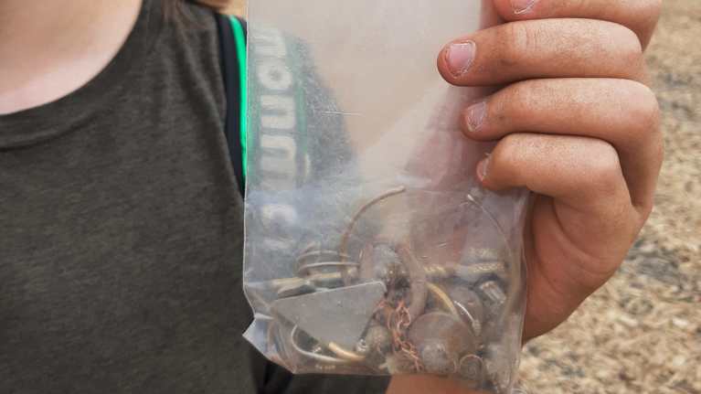 One hand held up a small plastic bag filled with coins, earrings, bracelets and other jewelry - items found on the beach after a rock festival.