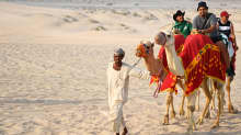 Turistit ratsastavat kamelilla hiekkarannalla.
