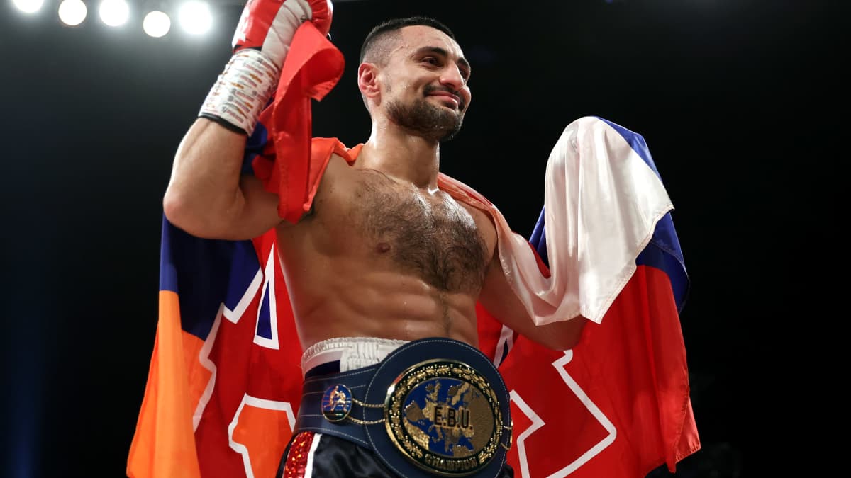 David Avanesyan hymyilee kädet pystyssä kietoutuneena jonkinlaiseen lippulakanaan.